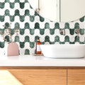 Bathroom with green and white geometric tile pattern, white bathtub, and wooden cabinet.