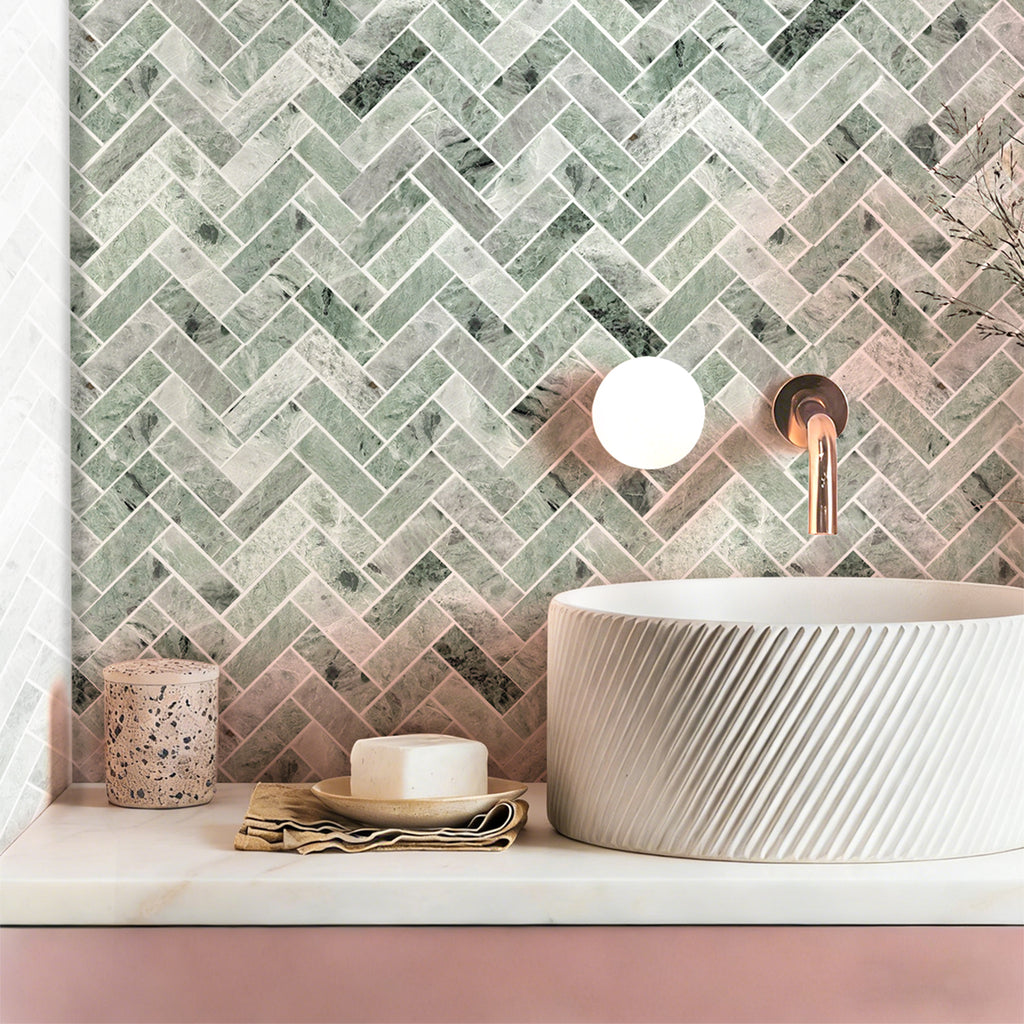 Bathroom with a green herringbone tile pattern on the wall, a white sink, and decorative items.