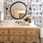 Bathroom vanity with round mirror, floral arrangement, and patterned wallpaper.